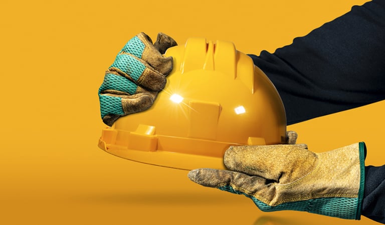 Hands with protective work gloves holding a yellow safety helmet